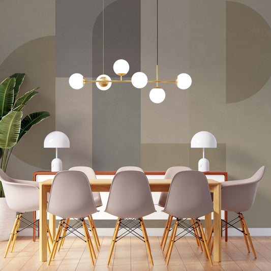cat-610512830792 A modern dining room featuring a wooden table surrounded by six light grey Eames-style chairs with wooden legs. A brass linear chandelier with six white globe bulbs hangs above the table. The background features a large-scale geometric wall mural in muted earth tones of sage, taupe, and beige, with two white mushroom-style table lamps sitting on a side console