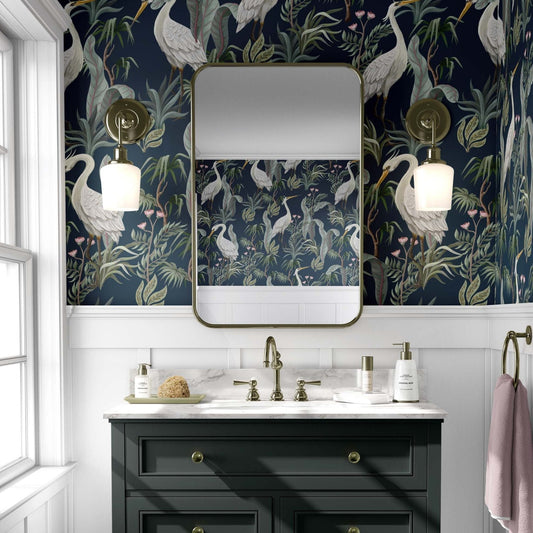 cat-610804236616 Dark navy wallpaper featuring white herons and tropical leaves installed in a modern bathroom with a gold mirror.