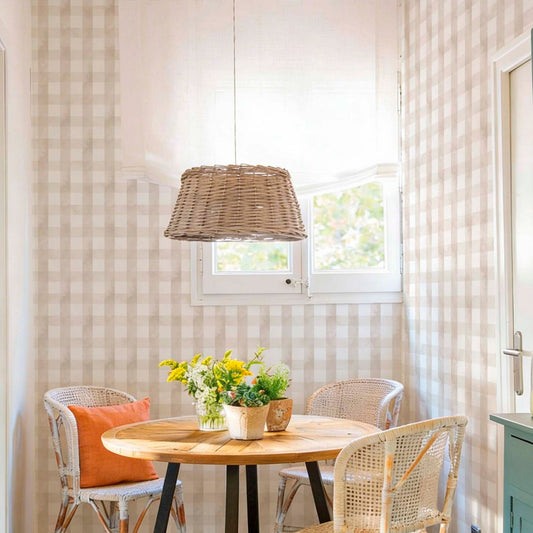 cat-659356549448   A cozy dining nook with walls covered in a neutral beige and white gingham wallpaper. The space features a round wooden table with a black metal base, woven rattan bistro chairs, and a large wicker pendant light hanging above.