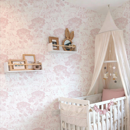 Cozy nursery interior featuring pink woodland animals Toile wallpaper, a white wooden crib with a canopy, and floating shelves with wooden toys.