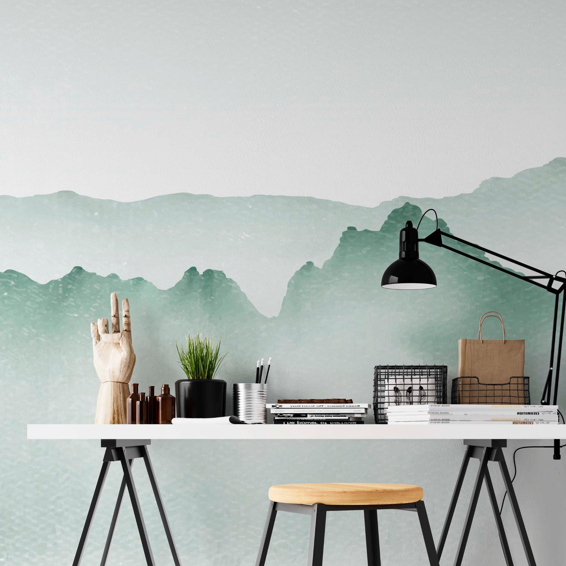 cat-660961526088 Decorative wallpaper featuring soft green watercolor mountains on a home office wall behind a white desk with black trestle legs and a black lamp.
