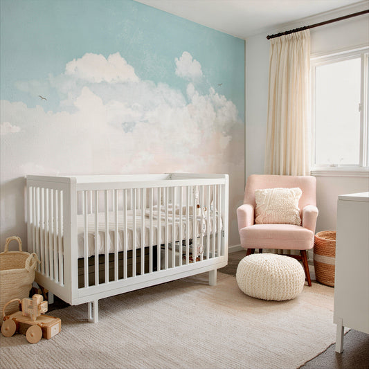 cat-610568044872 Pastel sky and clouds wallpaper mural in a nursery with white crib, blush pink armchair and woven baskets