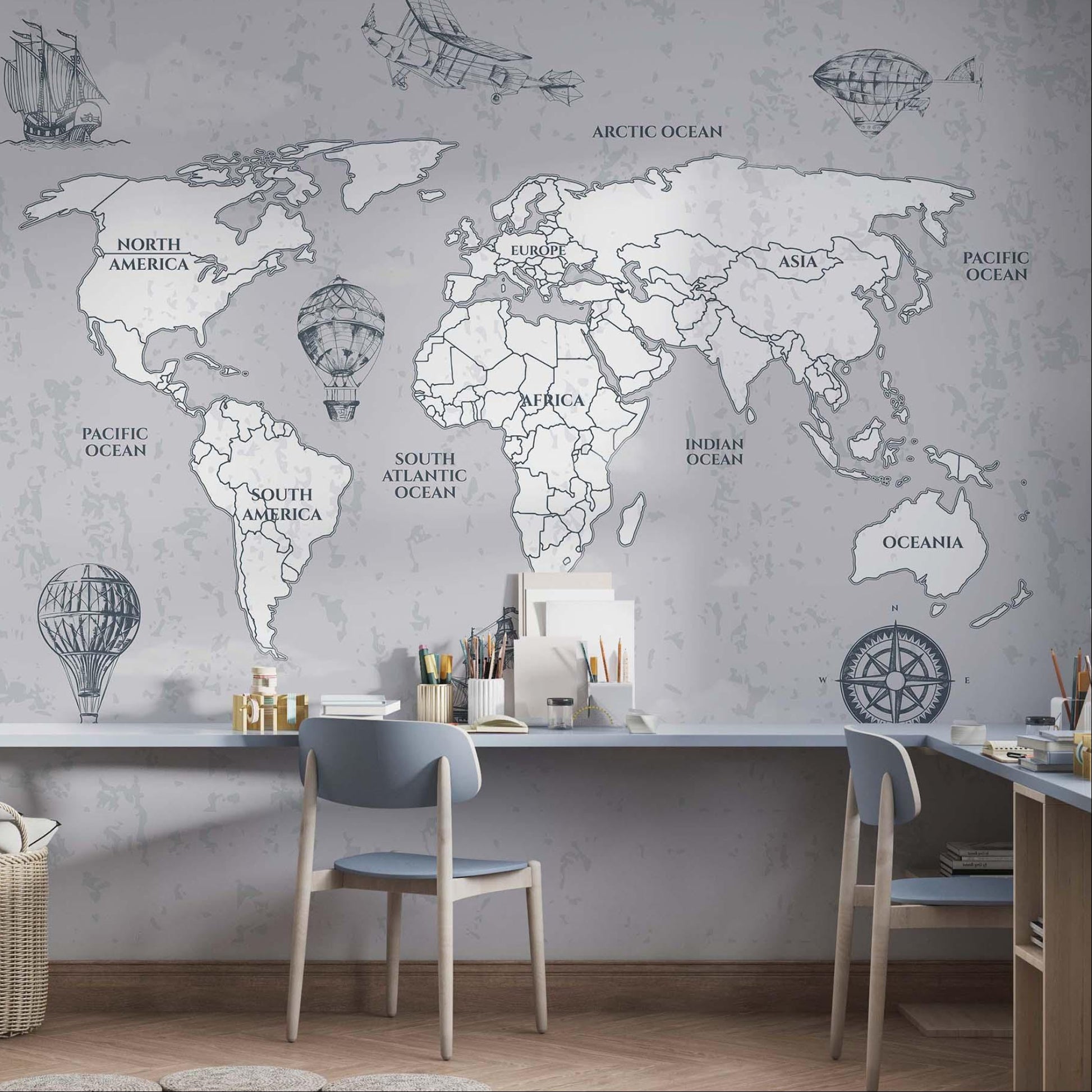 Vintage grey mapamundi wallpaper covering a long study wall above a shared floating desk with two wooden chairs, organizers, and a woven storage basket.