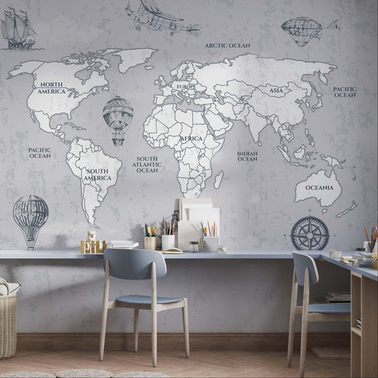 Vintage grey mapamundi wallpaper covering a long study wall above a shared floating desk with two wooden chairs, organizers, and a woven storage basket.