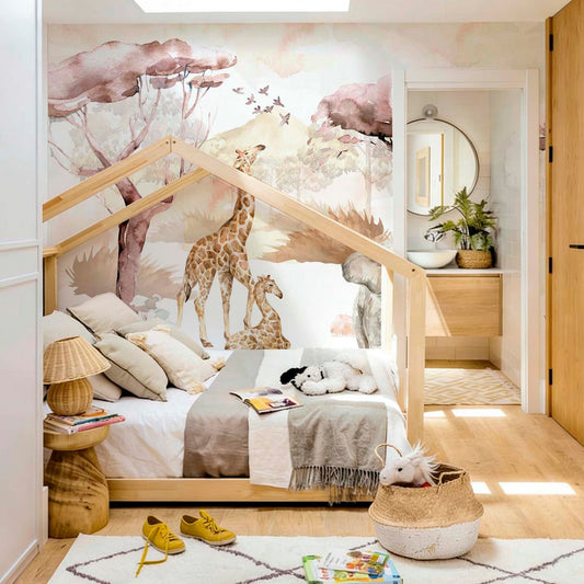 cat-661212758344 A children's bedroom featuring a safari watercolor wallpaper mural with giraffes behind a wooden house-shaped Montessori bed, styled with a plush rug and wicker baskets