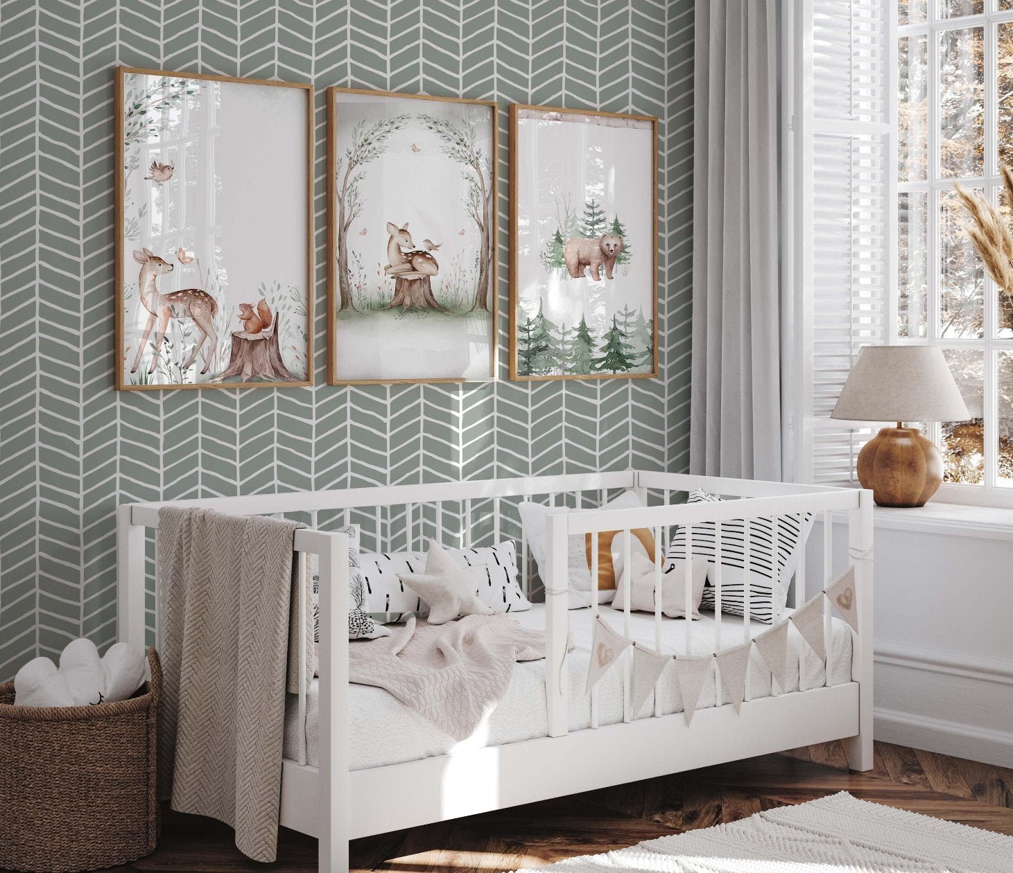 cat-615198294344 Nursery wall featuring a sage green and white hand-drawn herringbone wallpaper, styled with three animal-themed framed prints, a white wooden toddler bed, and a brown wicker basket.
