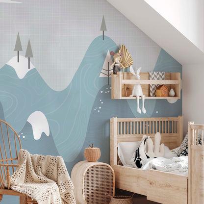 Snowy mountains nursery mural wallpaper in blue and grey tones in a nursery with wooden crib, rattan chair and natural wood shelf