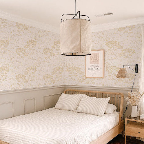 cat-616983200072 Cozy bedroom interior featuring soft yellow floral bouquet wallpaper above a light grey wainscoted wall, styled with a light wood bed frame, striped bedding, and a large fabric pendant light.
