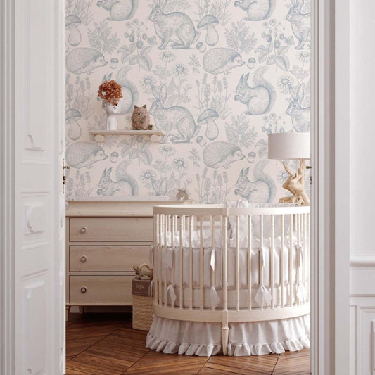 A serene nursery featuring soft, neutral tones with a round wooden crib draped in white linens. The walls are adorned with whimsical wallpaper depicting forest animals like squirrels, rabbits, and hedgehogs surrounded by flowers and mushrooms. A wooden dresser and a small shelf with decorative animal figurines add charm to the cozy space.