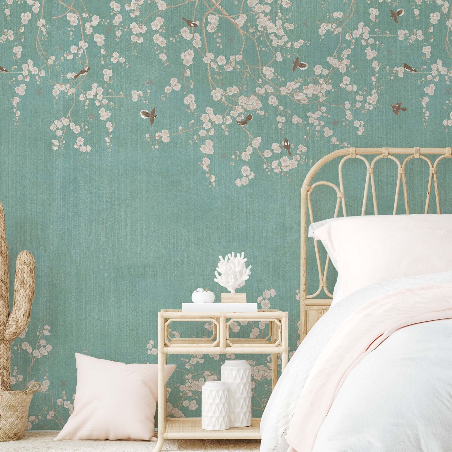 Boho-style bedroom featuring a teal wallpaper mural with white blossom branches and birds, a rattan headboard, and a light-wood nightstand with decorative coral.