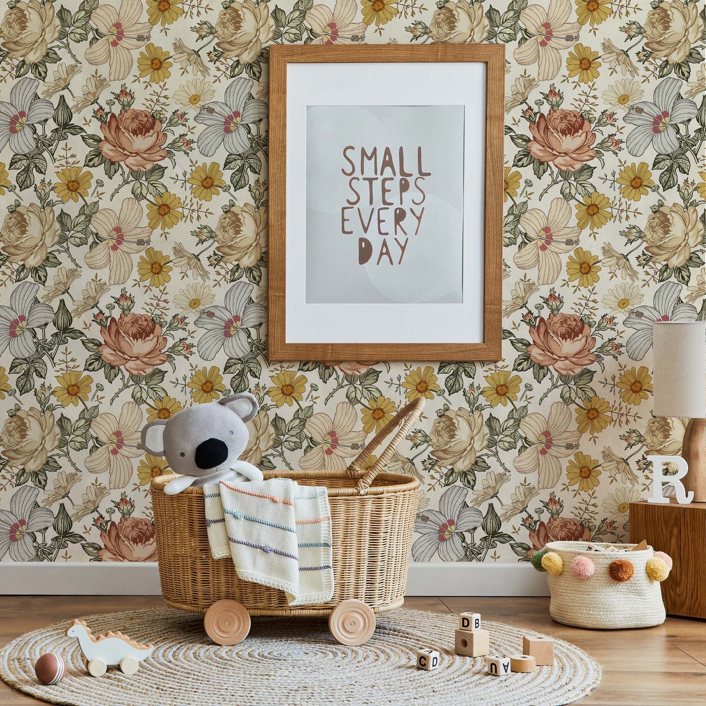 Cozy nursery with vintage floral wallpaper in yellow and pink, a wooden frame with the quote "Small steps every day," a rattan basket on wheels with a koala plush, and a round jute rug