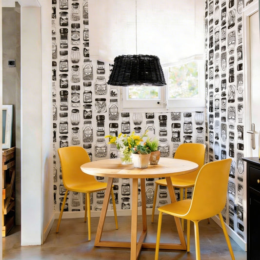 Modern dining area featuring vintage spice jar illustration wallpaper, a round light wood table with two bright yellow chairs, and a black wicker pendant light hanging above.