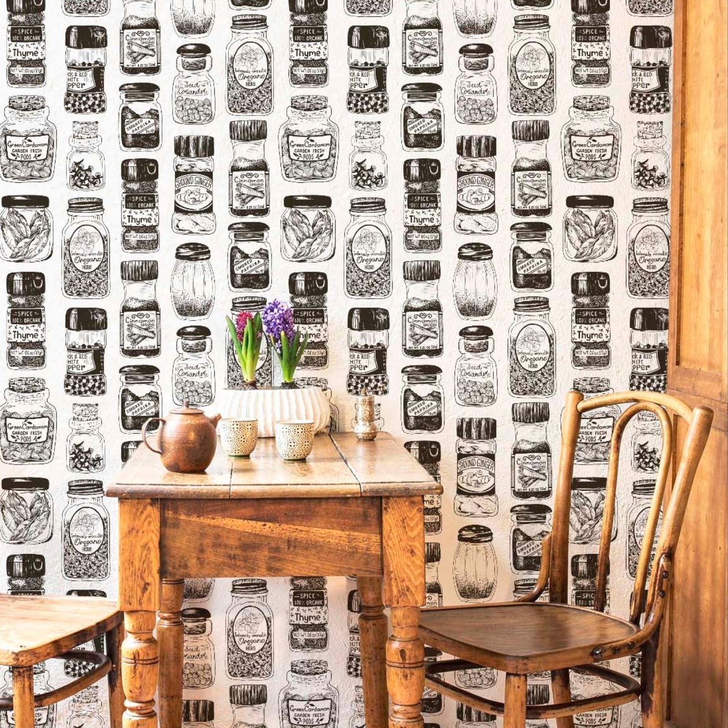 cat-615198490952 Rustic dining nook featuring vintage spice jar illustration wallpaper, a heavy antique wooden table with a teapot and flowers, and two matching wooden chairs.