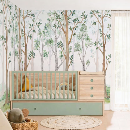 A nursery corner featuring a watercolor forest wallpaper mural with green trees behind a light wood and mint green convertible crib, styled with a round jute rug and a sheer white curtain.