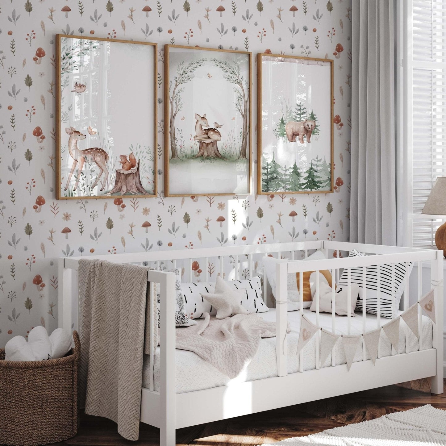 A bright nursery featuring watercolor mushroom wallpaper with red toadstools and forest leaves on a white background. Three framed forest animal prints hang above a white wooden crib, complemented by a wicker basket and neutral textiles.
