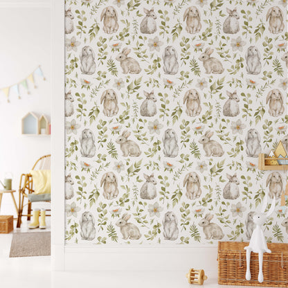 Whimsical nursery wallpaper featuring hand-painted bunnies, green leaves, and white flowers in a bright room with a wicker chest and white rabbit decor