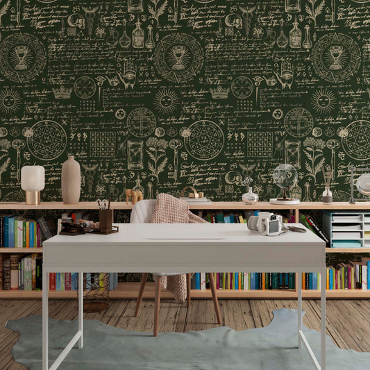 Modern white desk and bookshelves in front of a dark green wall with cream-colored alchemy illustrations, sketches, and mystical symbols.