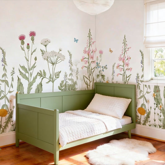 Large scale floral wallpaper mural featuring illustrated wildflowers, pink foxgloves, and thistles on a white background in a child's bedroom with a green bed.