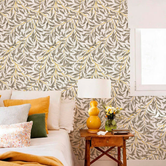 Bedroom with Willow Leaf wallpaper featuring trailing botanical leaves in soft olive and mustard tones, styled with warm textiles and natural wood furniture.