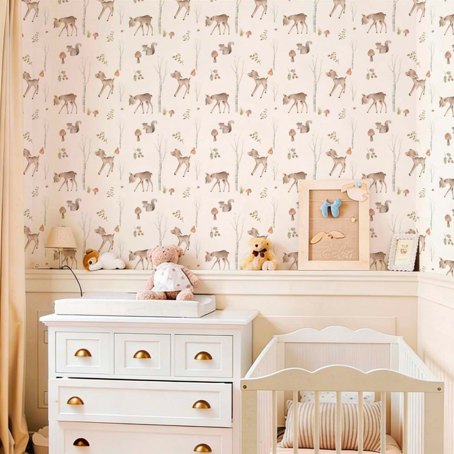 Sweet nursery featuring woodland-themed wallpaper with deer, squirrels, and birch trees, a white dresser with gold handles, a matching white crib, and various stuffed animals like a teddy bear.