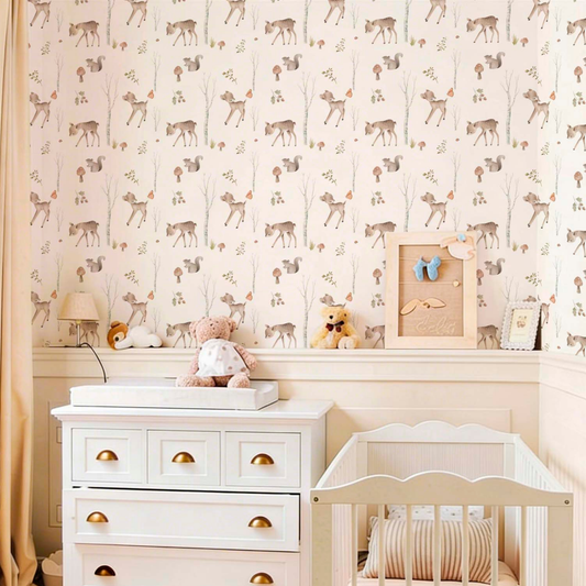 Sweet nursery featuring woodland-themed wallpaper with deer, squirrels, and birch trees, a white dresser with gold handles, a matching white crib, and various stuffed animals like a teddy bear.
