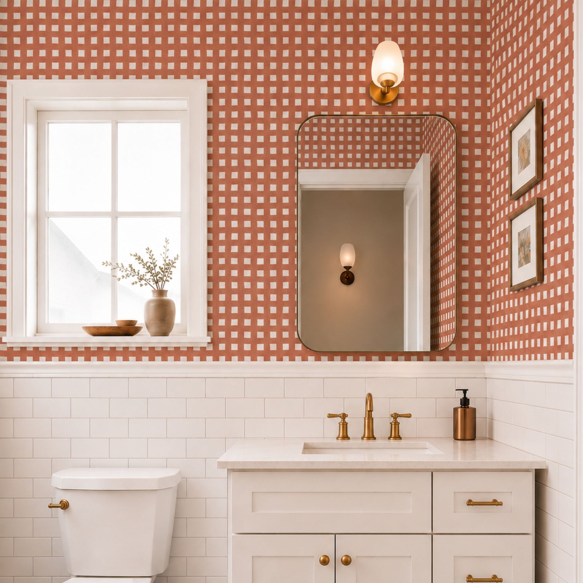 cat-610804236616 Terracotta check wallpaper in a bright bathroom with white subway tiles, a white vanity, brass fixtures and warm natural light.