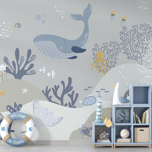 Decorative kids wallpaper featuring an illustrated light grey and blue underwater scene with a whale next to a blue wooden shelving unit with nursery decor.